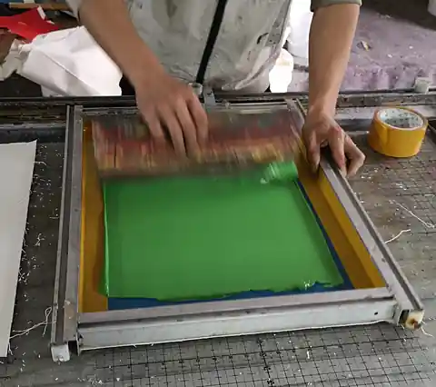 Sérigraphie en atelier Sérigraphie d'un sac en toile dans l'atelier de fabrication : passage de la racle sur l'écran
